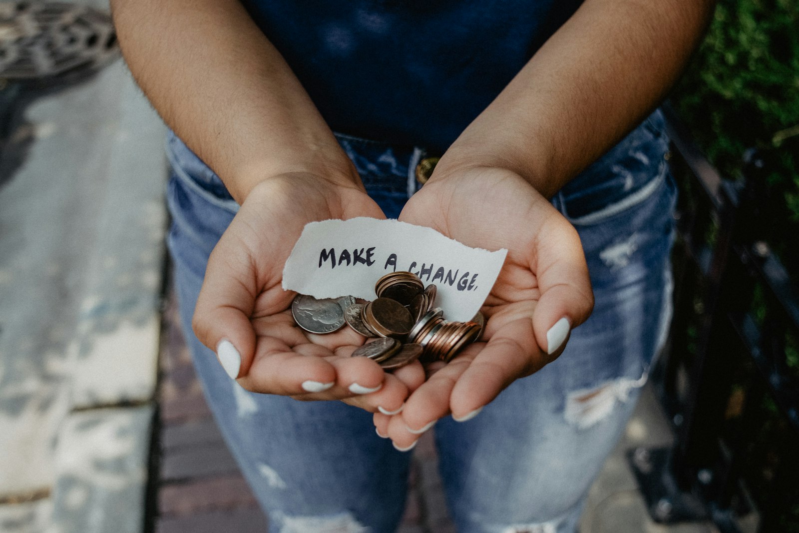 Hands holding a handwritten sign and coins, symbolizing community fundraising and giving
